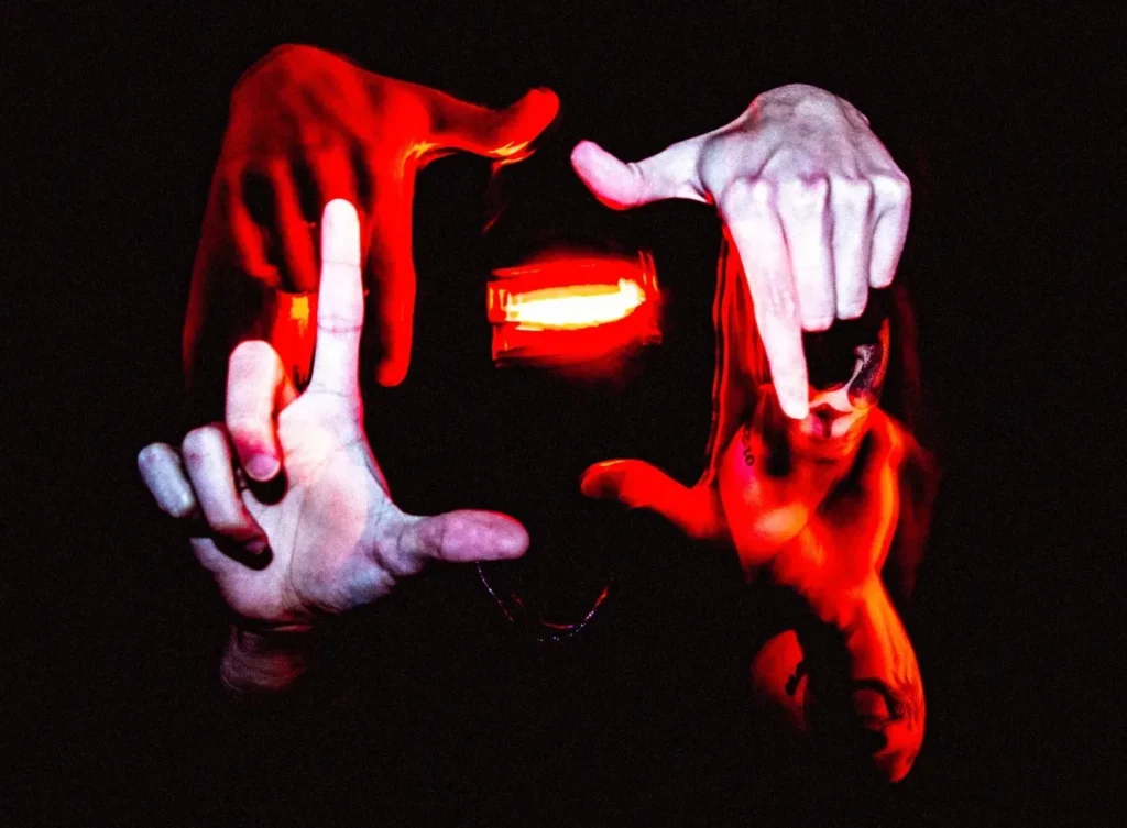 Mains encadrant une lumière rouge en arrière-plan, ambiance artistique intense