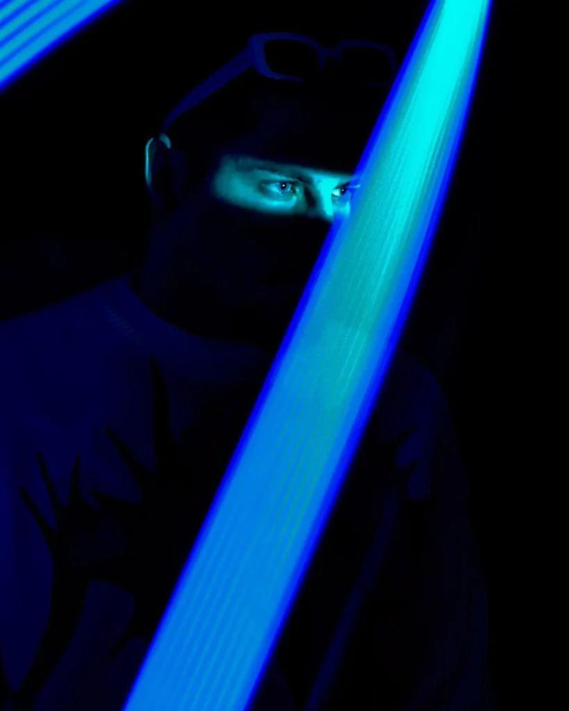 Portrait sombre d’un homme à moitié dissimulé derrière une lumière bleue en mouvement, réalisé par Lo_garithme.