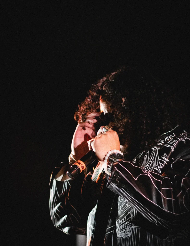 Portrait rapproché d’un chanteur sur scène ajustant ses lunettes, capturé dans un contraste fort par Lo_garithme.