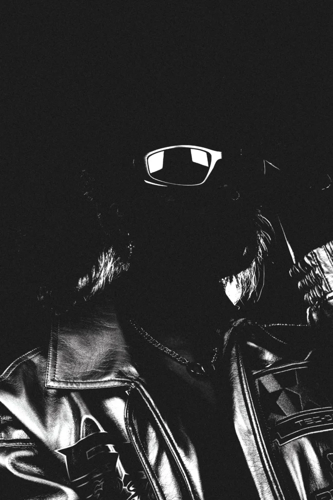 Portrait en noir et blanc d’un homme en lunettes et blouson brillant, style urbain underground.