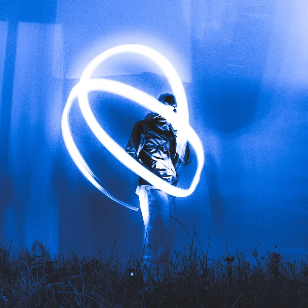 Personne en blouson métallique entourée de traînées lumineuses blanches sur fond bleu nocturne